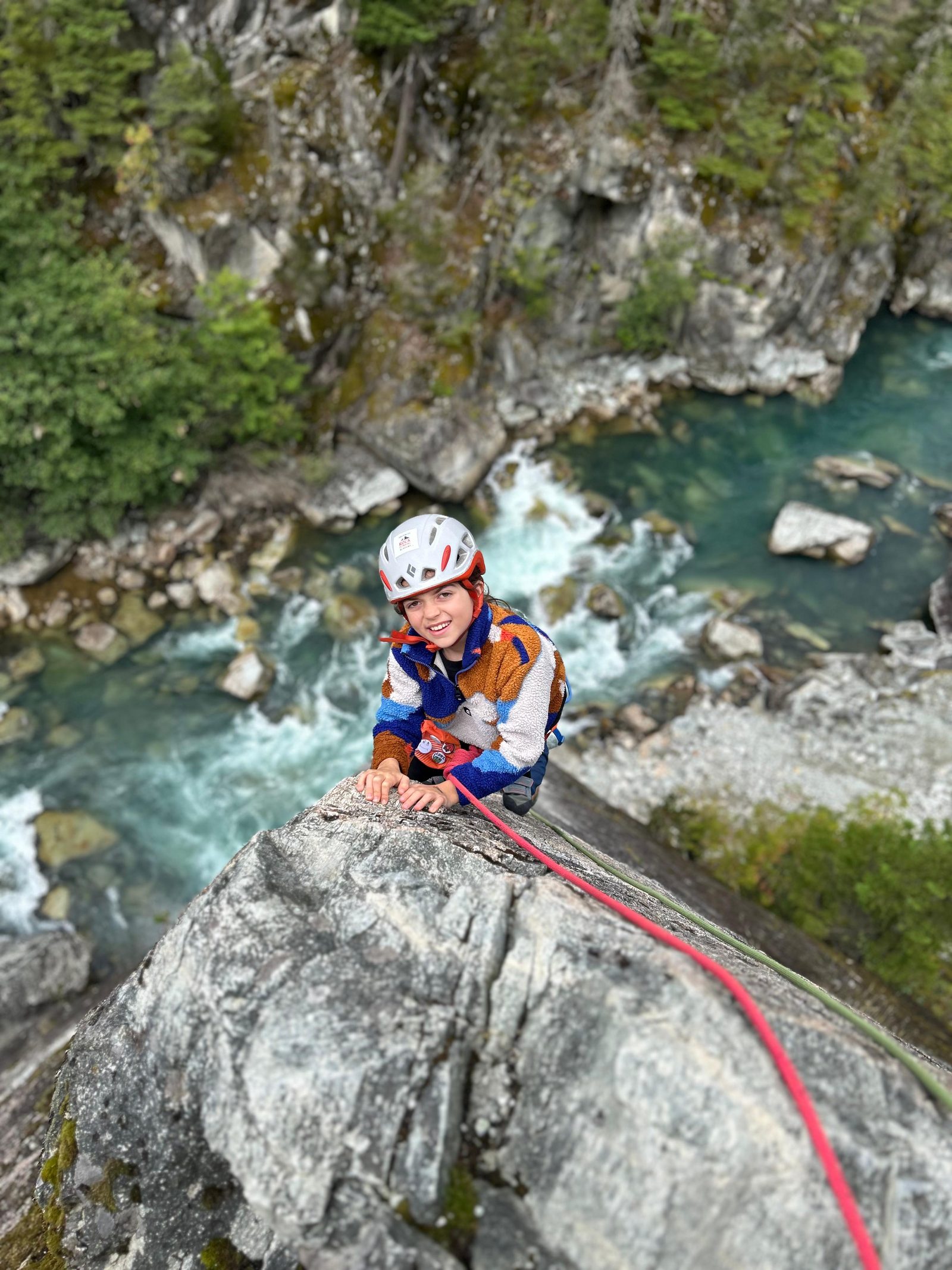 Alice in a white helmet and striped fleece at the lip of a granite boulder above the river in Squamish, with a pink rope and a green rope beside her.