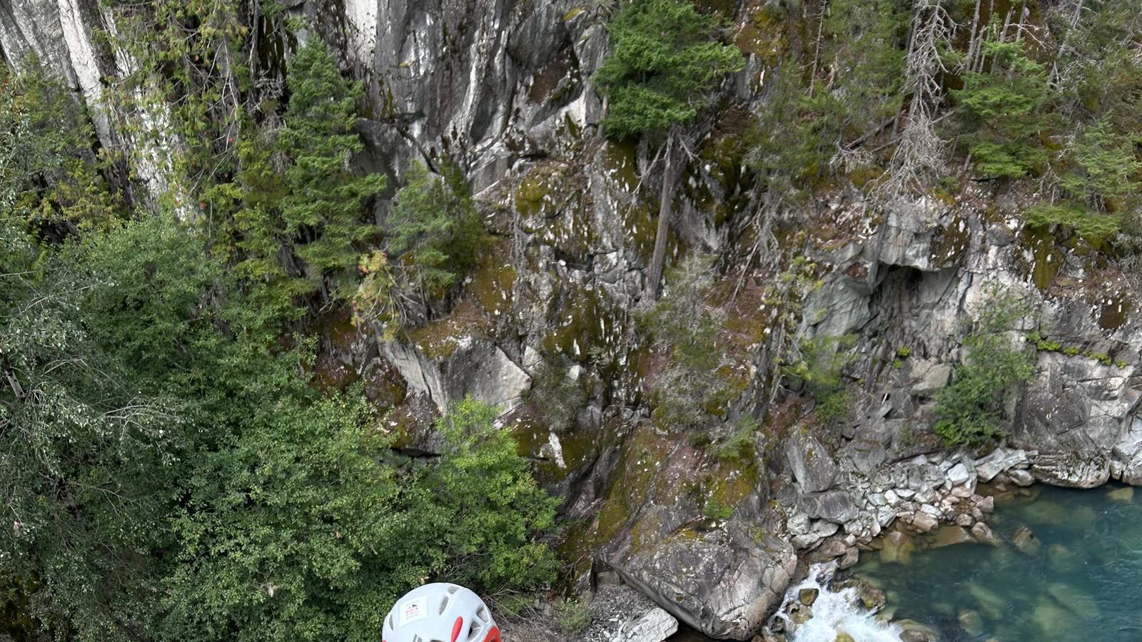 Alice and Keith on a granite slab above a river in Squamish, wearing climbing helmets, with a pink rope and a green rope running down the rock.